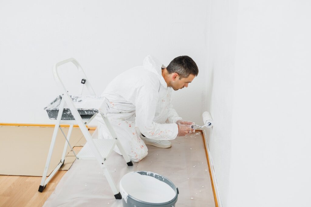 Man doing house renovation. Industrial theme. Painting walls. Builder in white overalls paints wall